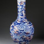 Vase of porcelain, with bulbous body and long straight neck. Painted under a clear glaze with four dragons in blue outline and a pearl among clouds in red, on a cloudy blue ground.