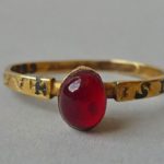 Amulet-ring; gold; slender flat hoop with nielloed inscription; raised oval bezel containing ruby.